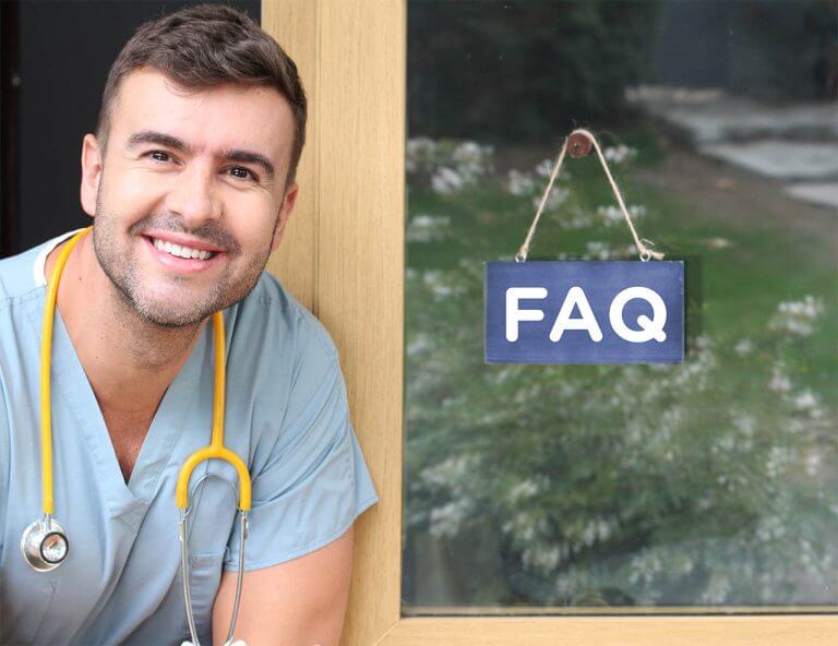 Smiling male nurse sitting next to window with FAQ sign hanging