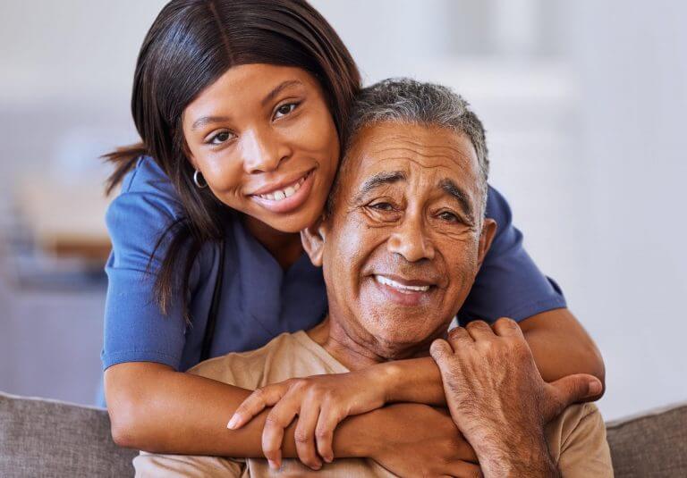 Caring smiling nurse hugging older male patient from behind