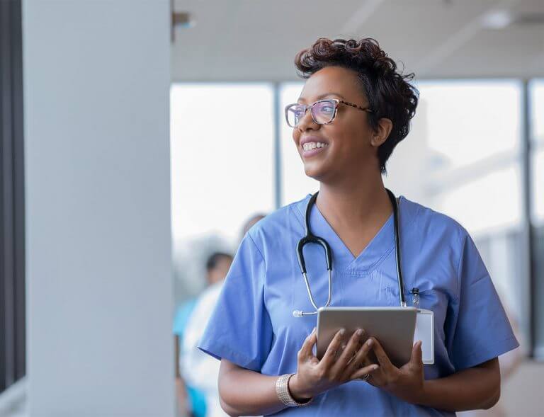 Female nurse holding digital tablet smiles while looking out window