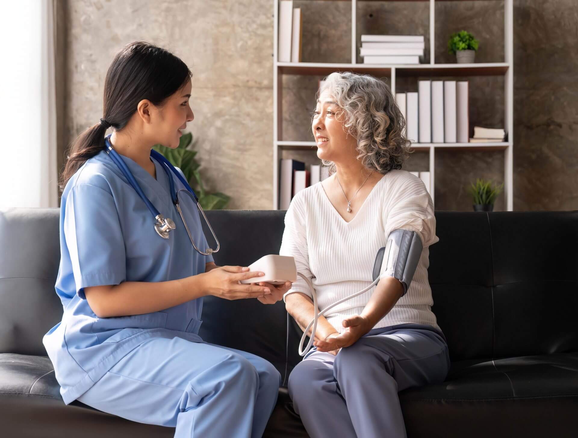 Nurse sitting on couch with female patient taking her blood pressure.