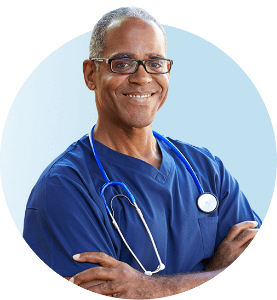 Male hematologist standing in blue scrubs with arms folded smiling