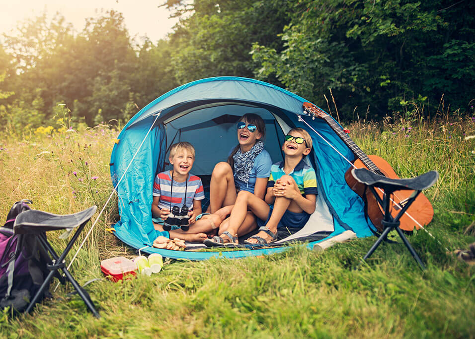 Children camping in blue tent laughing and smiling