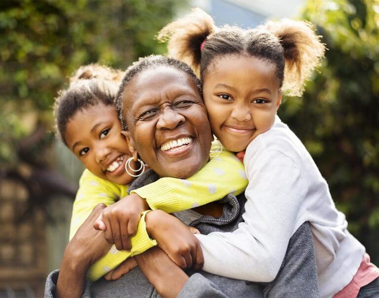 Older woman getting big hugs from granddaughters