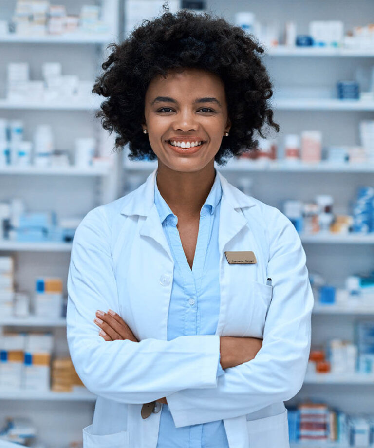 Female pharmacy manager standing smiling with arms folded in front of drug supply closet.