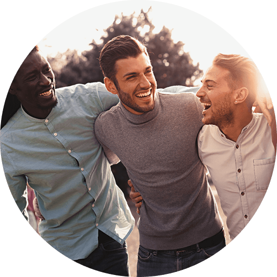 Group of three men walking arm in arm smiling at sunset.