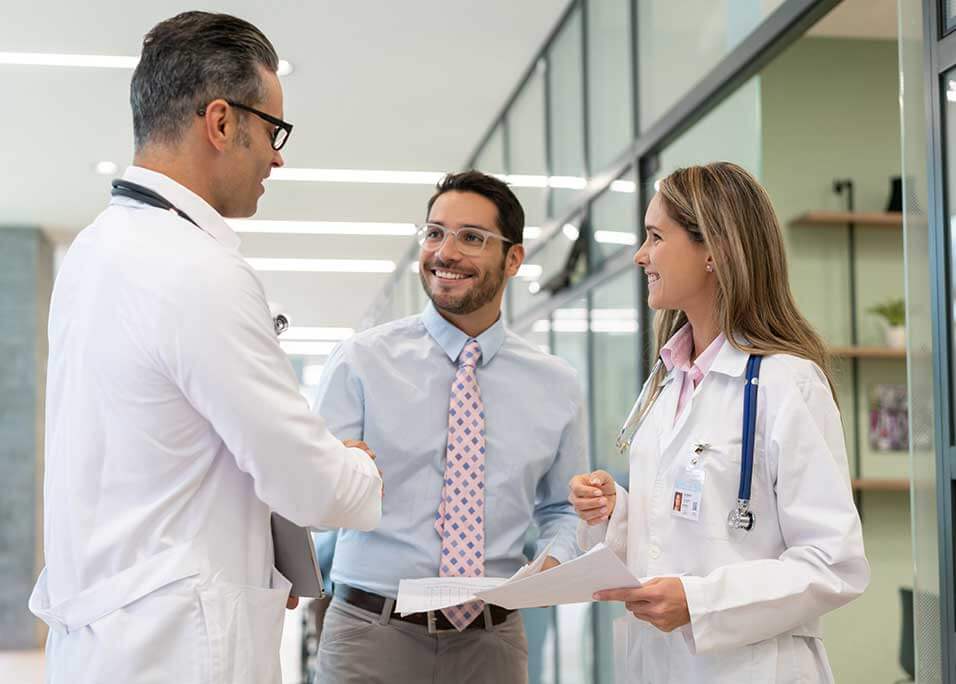 Business man talking to two doctors in a hospital smiling and shaking hands