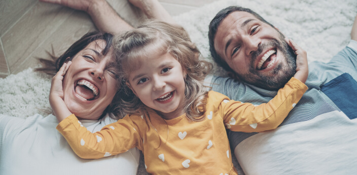 Parents with young daughter lying on a rug and smiling